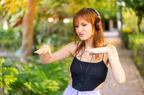 Young pretty redhead woman at outdoors listening music and dancing