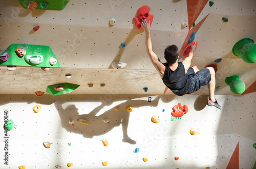Young man bouldering in indoor climbing gym, with clear shadow on wall