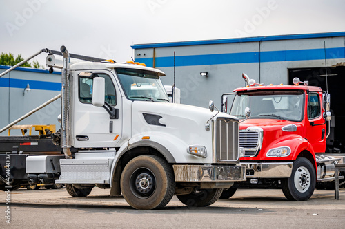 Two skid-mounted big rigs day cab semi trucks for transporting waste containers are parked in a warehouse awaiting another order