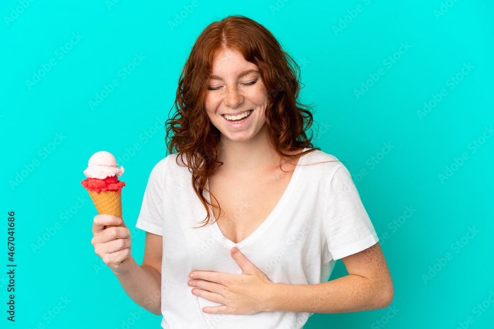 Teenager reddish woman with a cornet ice cream isolated on blue background smiling a lot Teenager reddish woman with a cornet ice cream isolated on blue background smiling a lot