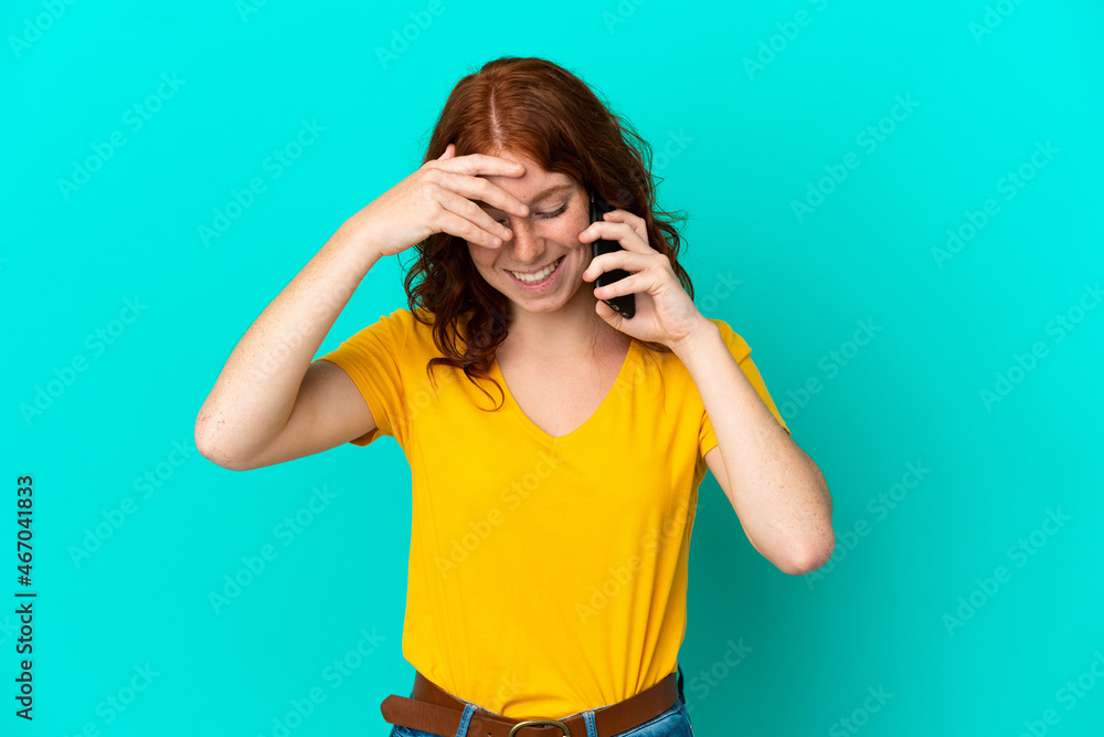 Teenager reddish woman using mobile phone isolated on blue background laughing Teenager reddish woman using mobile phone isolated on blue background laughing