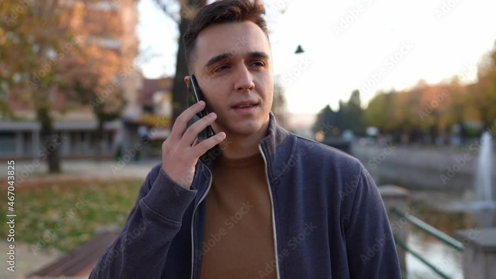 One Young happy caucasian man standing outdoor alone in autumn evening making a phone call smiling happy talking front view close up real people One Young happy caucasian man standing outdoor alone in autumn evening making a phone call smiling happy talking front view close up real people