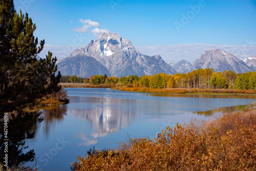 Grand Tetons reflected in blue lake with autumn colors in Wyoming