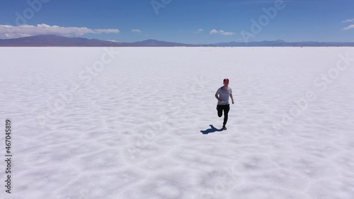 Young man running in the middle of the great salt flats of Jujuy in Argentina. Aerial drone 4K video. Sport and travel concept. photo