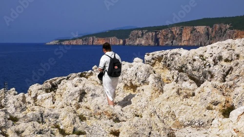 Woman In White Dress Walking On The Rocky Seashore Of Alaties Beach In Erisos, Greece. wide shot photo