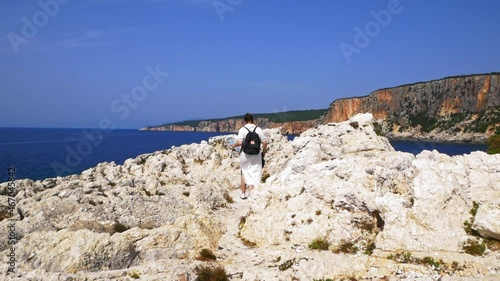 Back View Of A Woman With Backpack Walking On White Rocks At Alaties Beach In Erisos, Kefalonia, Greece At Summer. wide photo