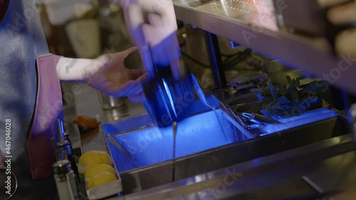 A bartender prepares his drink by adding ice cubes into the shaker photo