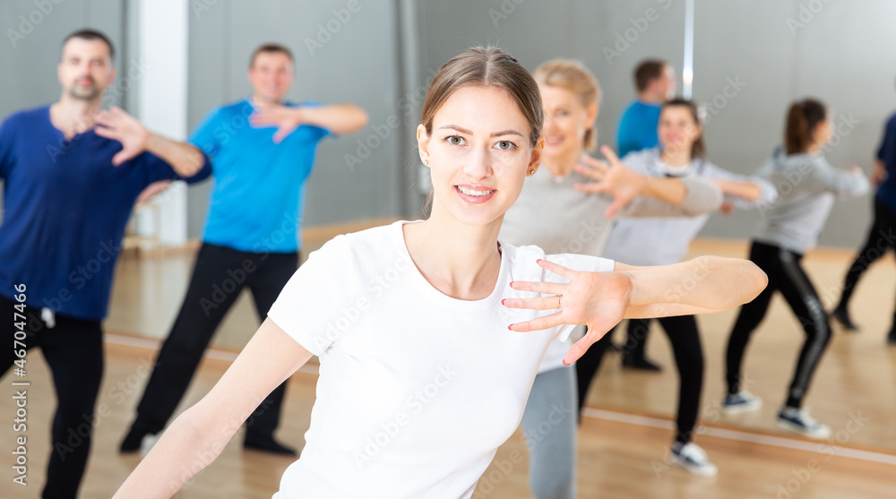 Portrait of young emotional woman doing exercises during group class in dance center