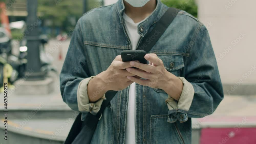Close Up Asian man wearing a surgical mask and using a smartphone while walking on the street in the city during the covid-19 pandemic. Close Up Asian man wearing a surgical mask and using a smartphone while walking on the street in the city during the covid-19 pandemic.