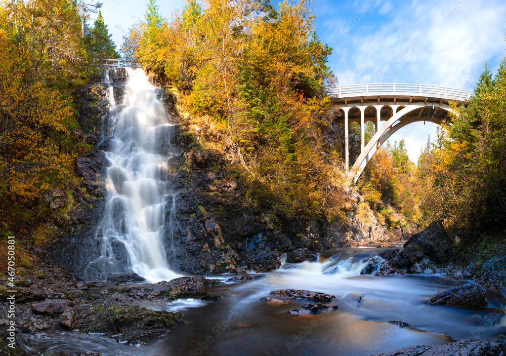 A bridge crosses the river as a waterfall flows into it in autumn A bridge crosses the river as a waterfall flows into it in autumn