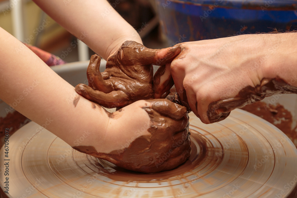The child moulds from clay a pot on a potter's wheel. Adults help the child to work with clay.