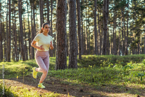 Fototapeta Naklejka Na Ścianę i Meble -  Front view full length of one young caucasian woman running trough the woods in nature outdoor jogging in sunny day - sport fitness and recreation concept copy space