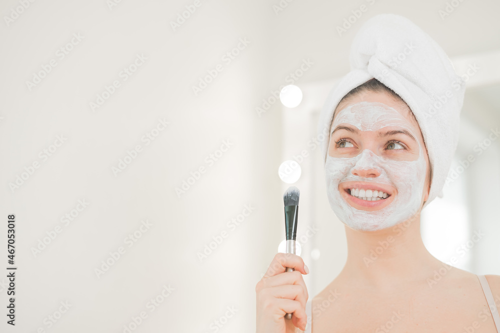 Beautiful caucasian woman with a towel on her hair applies a clay face mask. Taking care of beauty at home Beautiful caucasian woman with a towel on her hair applies a clay face mask. Taking care of beauty at home