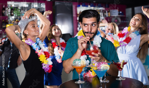 Young smiling man is drinking cocktail on hawaiian party in bar.