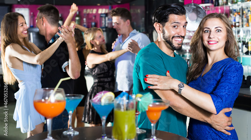 Young cheerful women with men are dancing in pairs on the dance floor in the nightclub