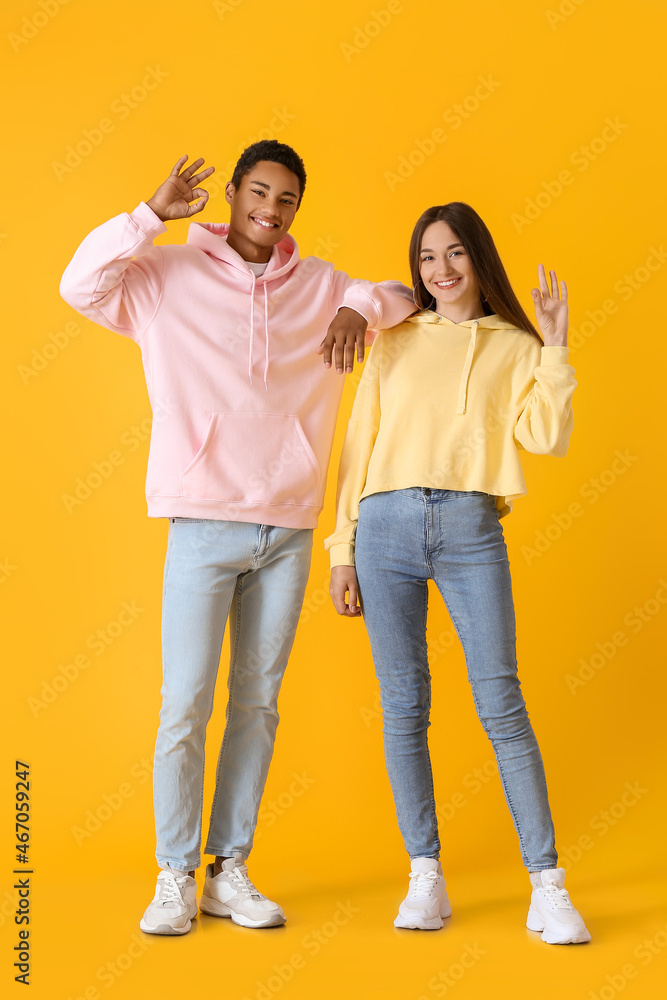 Fototapeta premium Stylish young couple in hoodies showing OK on yellow background