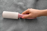Woman cleaning grey cloth with lint roller, closeup