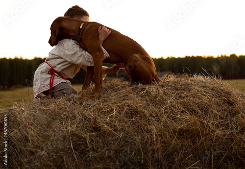 two boys sit near a haystack at sunset