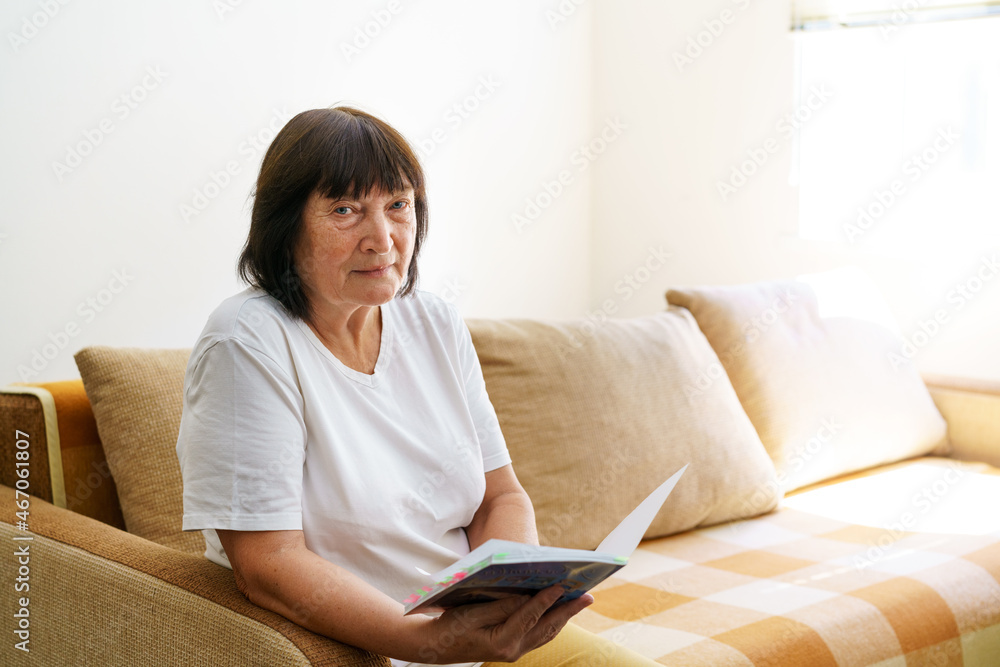 Portrait of attractive focused cheerful woman sitting on sofa reading book, pastime, dream at home home, apartment indoors during the day. Caucasian happy pensioner wearing casual clothes Portrait of attractive focused cheerful woman sitting on sofa reading book, pastime, dream at home home, apartment indoors during the day. Caucasian happy pensioner wearing casual clothes