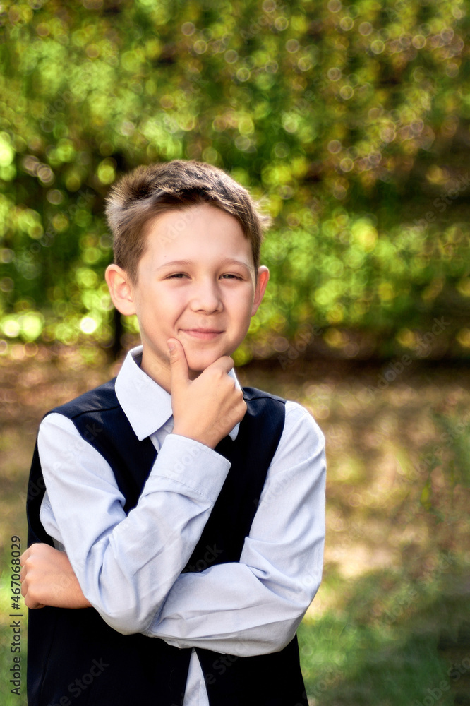 Portrait of a schoolboy looking thoughtfully to the side, against a blurry background of green trees. Portrait of a schoolboy looking thoughtfully to the side, against a blurry background of green trees.
