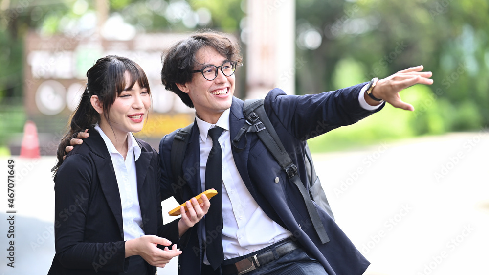 Two cheerful young business people talking to each other while standing outdoors at the city streets. Two cheerful young business people talking to each other while standing outdoors at the city streets.