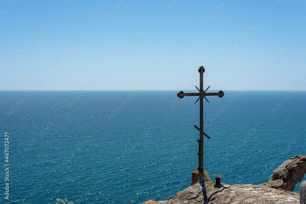Cross against a hothouse background of sea and sky.
