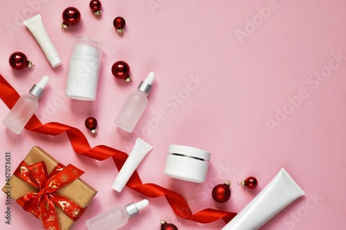 Set of cosmetic products. Winter cream for skin, skincare product, moisturizing cream with red christmas balls and gift box on pink background. Idea for winter shopping, presents. Top view. Copy space