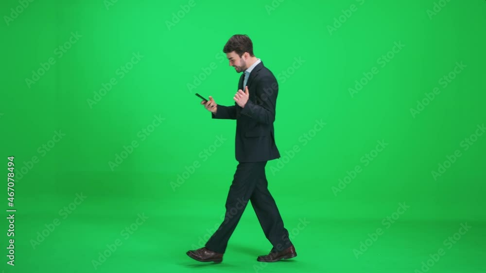 Passer-by businessman in a suit walks on a green background and uses a smartphone, man enjoys financial success and good news, template on a chromakey. Passer-by businessman in a suit walks on a green background and uses a smartphone, man enjoys financial success and good news, template on a chromakey.