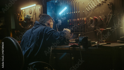Young blacksmith man with workwear, taking solder tool, sitting on chair and do solder.