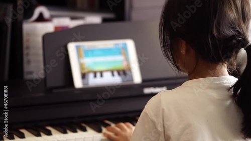 Asian girl is learning and practicing piano music using Online tablet Application to connect with keyboard using bluetooth.