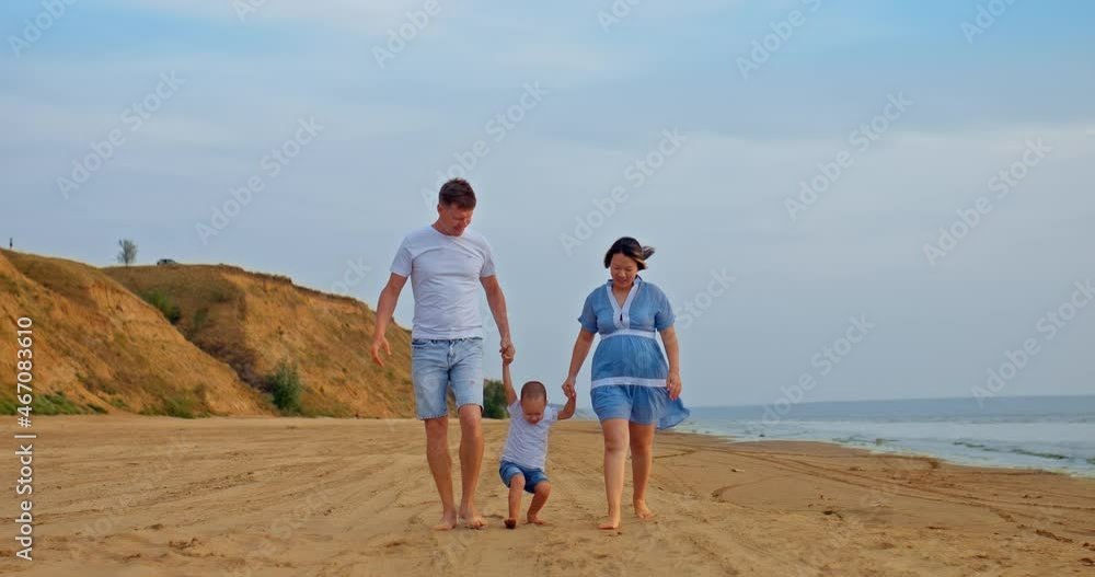 Pregnant woman with her husband and child walks along the seashore. Happy child with mother and father, parents lead the baby by the hands. Happy family is expecting a baby. 4k, ProRes Pregnant woman with her husband and child walks along the seashore. Happy child with mother and father, parents lead the baby by the hands. Happy family is expecting a baby. 4k, ProRes