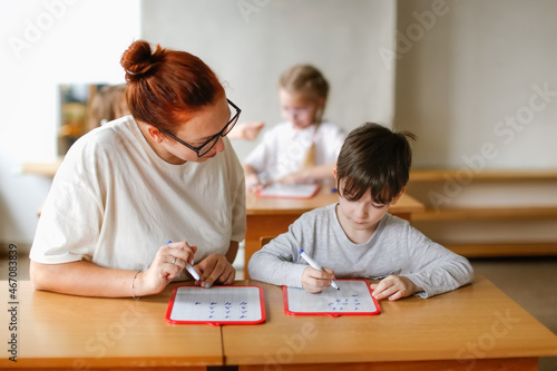 teacher and student at a school desk, the teacher explains and deals with the boy in the classroom, individual work. Light class, real class in a private school