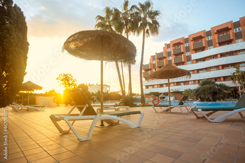 Photography of deck chair and umbrella and a pool  a residential area during the sunset with palms and pool