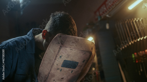 Foto Young blacksmith man with welding shield using welding machine for welding metal
