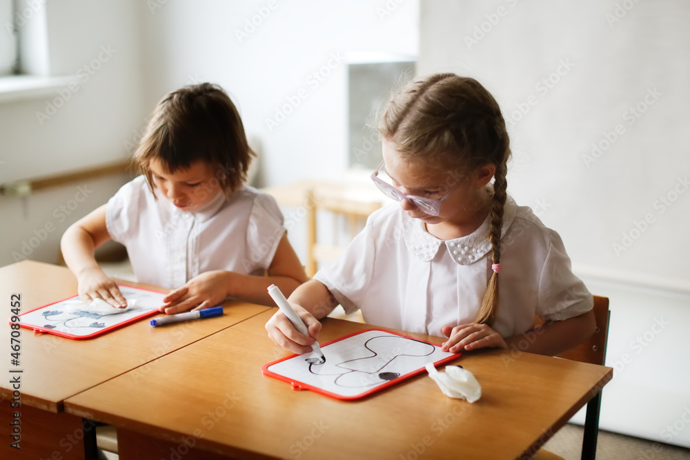 Cute caucasian girl child blonde with pigtails writes with a marker on a tablet, classes at school and independent work of children, light real class at school, soft focus and warm toning Cute caucasian girl child blonde with pigtails writes with a marker on a tablet, classes at school and independent work of children, light real class at school, soft focus and warm toning