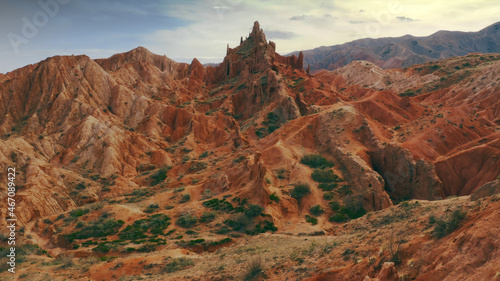 A magnificent aerial flight on a throne over a rocky red-orange canyon with green plants and rocks in the form of a fairy-tale castle. A fabulous aerial shot of a unique canyon landscape in Kyrgyzstan