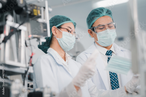 Both male and female Asian scientists are outfitted with protective gear. Examining the factory's machinery and materials used in the mask-making process. Covid 19 is a piece of preventive equipment.