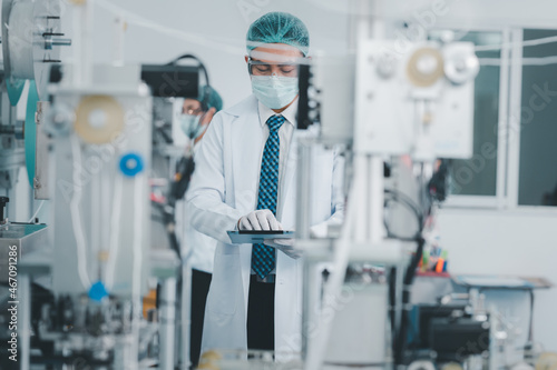 Both male and female Asian scientists are outfitted with protective gear. Examining the factory's machinery and materials used in the mask-making process. Covid 19 is a piece of preventive equipment.