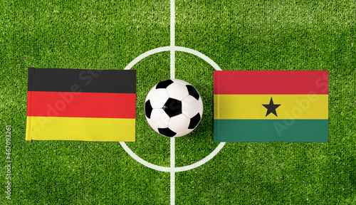 Top view soccer ball with Germany vs. Ghana flags match on green football field.