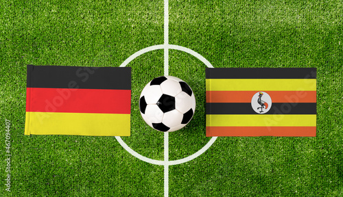 Top view soccer ball with Germany vs. Uganda flags match on green football field.