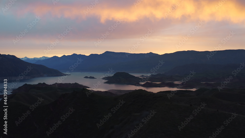 Aerial landscape with beautiful bright yellow-orange clouds in the dawn sky and a large lake and silhouettes of mountains Idyllic panoramic landscape with river and island and mountains, violet sunset