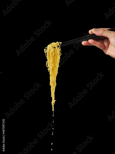 Hand holding chopsticks and noodles on black background