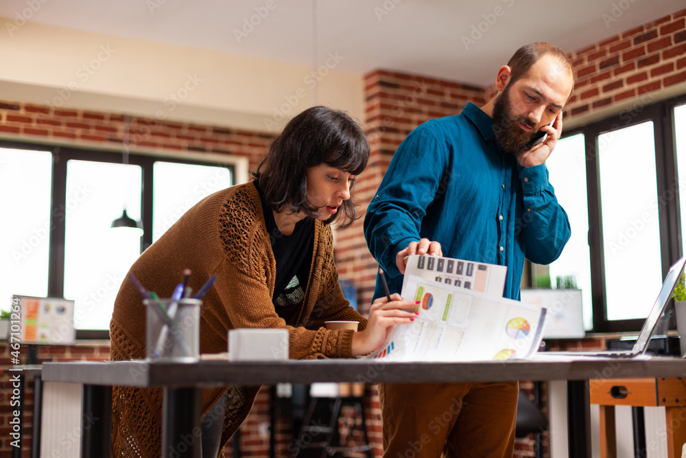 Businessman talking at phone with manager discussing company strategy while working at marketing presentation with entrepreneur woman in startup office. Businesspeople analyzing business document Businessman talking at phone with manager discussing company strategy while working at marketing presentation with entrepreneur woman in startup office. Businesspeople analyzing business document