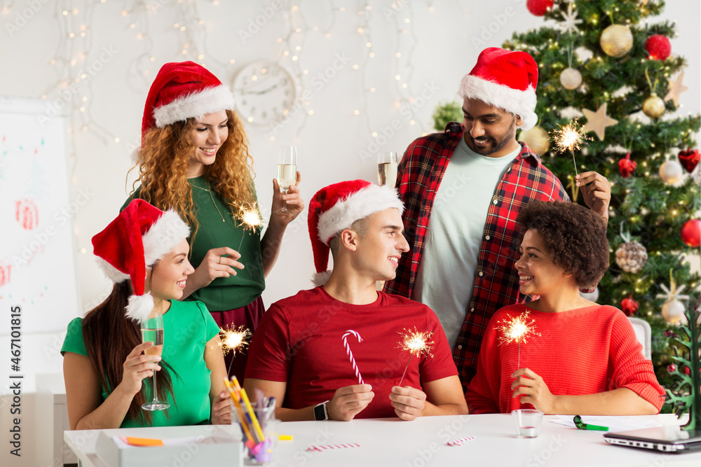 celebration and winter holidays concept - team in santa hats with sparklers and non-alcoholic sparkling wine at corporate office party over christmas tree background
