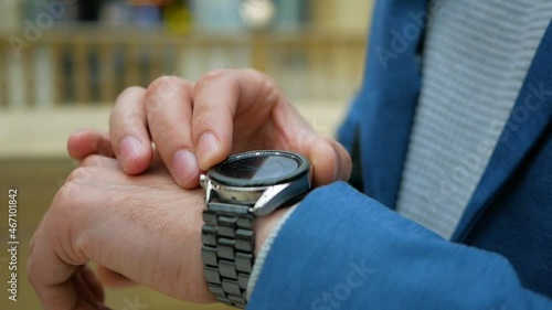A young man in office clothes uses a smart watch in a business center. Concept of modern metropolis and business relations 