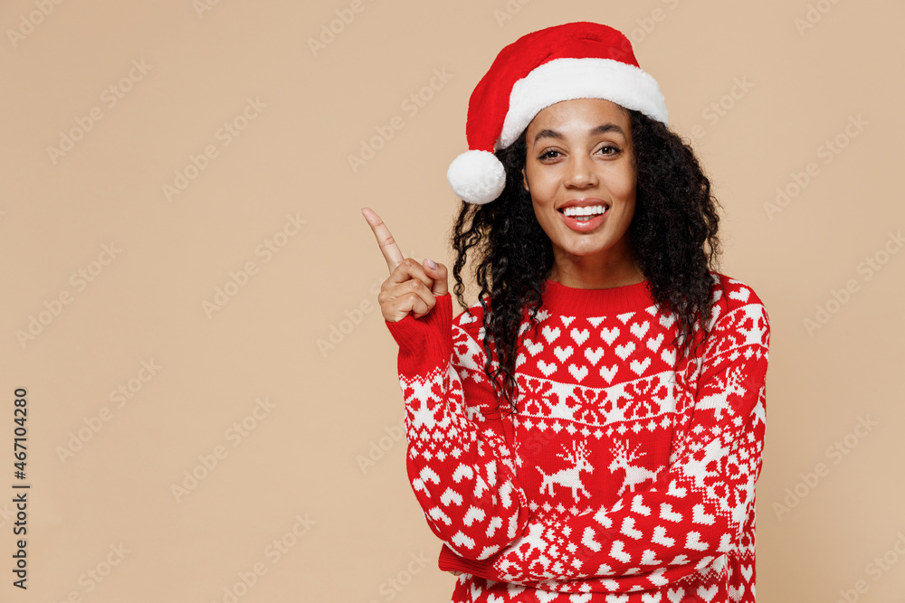 Fun young african american Santa woman in Christmas hat sweater pointing on workspace area copy space mock up isolated on pastel beige background studio portrait. Happy New Year x-mas holiday concept. Fun young african american Santa woman in Christmas hat sweater pointing on workspace area copy space mock up isolated on pastel beige background studio portrait. Happy New Year x-mas holiday concept.