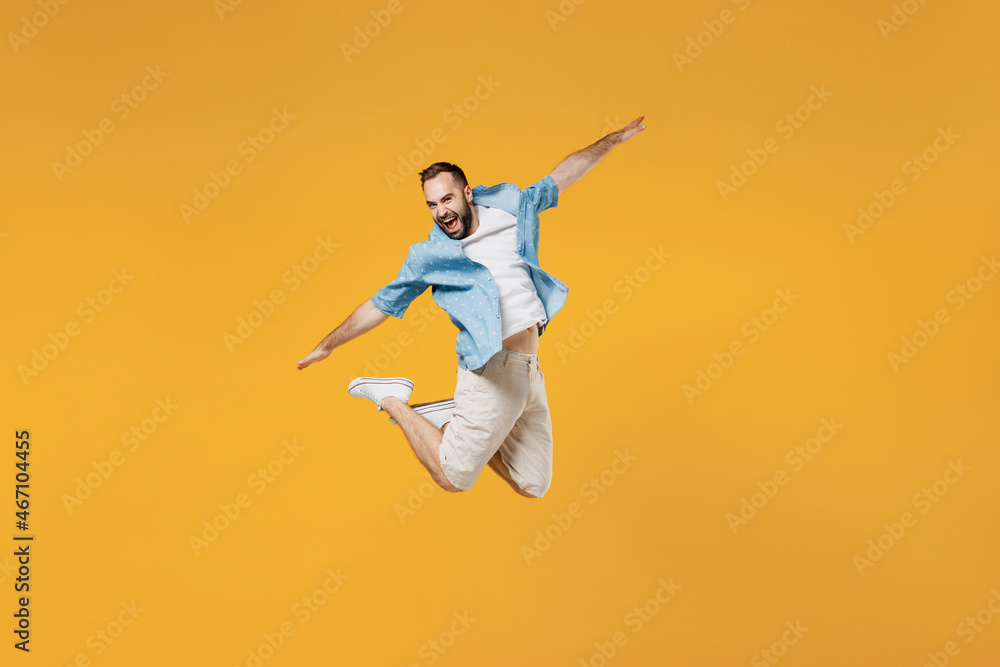 Full body young smiling happy man 20s wear blue shirt white t-shirt jump high with outstretched hands like flying scream isolated on plain yellow background studio portrait. People lifestyle concept.