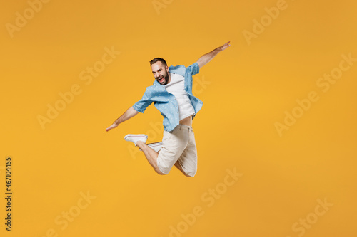 Full body young smiling happy man 20s wear blue shirt white t-shirt jump high with outstretched hands like flying scream isolated on plain yellow background studio portrait. People lifestyle concept.