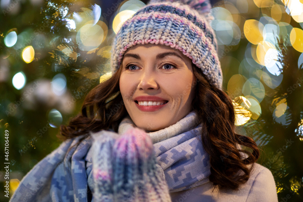 winter holidays and people concept - portrait of happy smiling young woman in hat, mittens and scarf over christmas lights winter holidays and people concept - portrait of happy smiling young woman in hat, mittens and scarf over christmas lights
