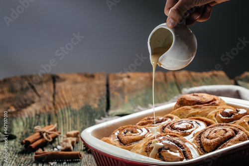 Homemade Cinnamon roll. Woman's hand spreading vanilla icing freshly baked cinnamon rolls photo